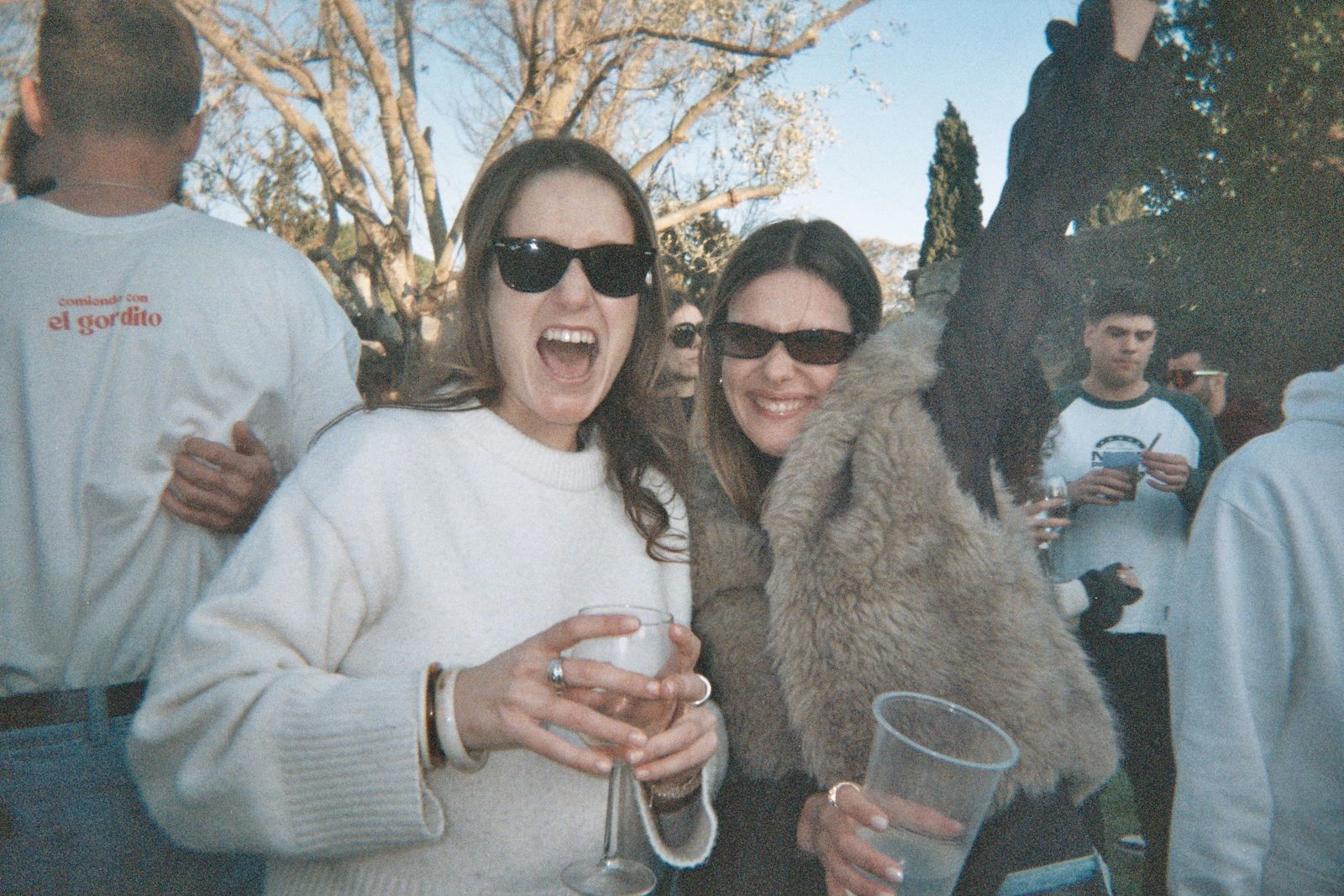Dos invitadas riéndose con una copa de vino en un evento al aire libre